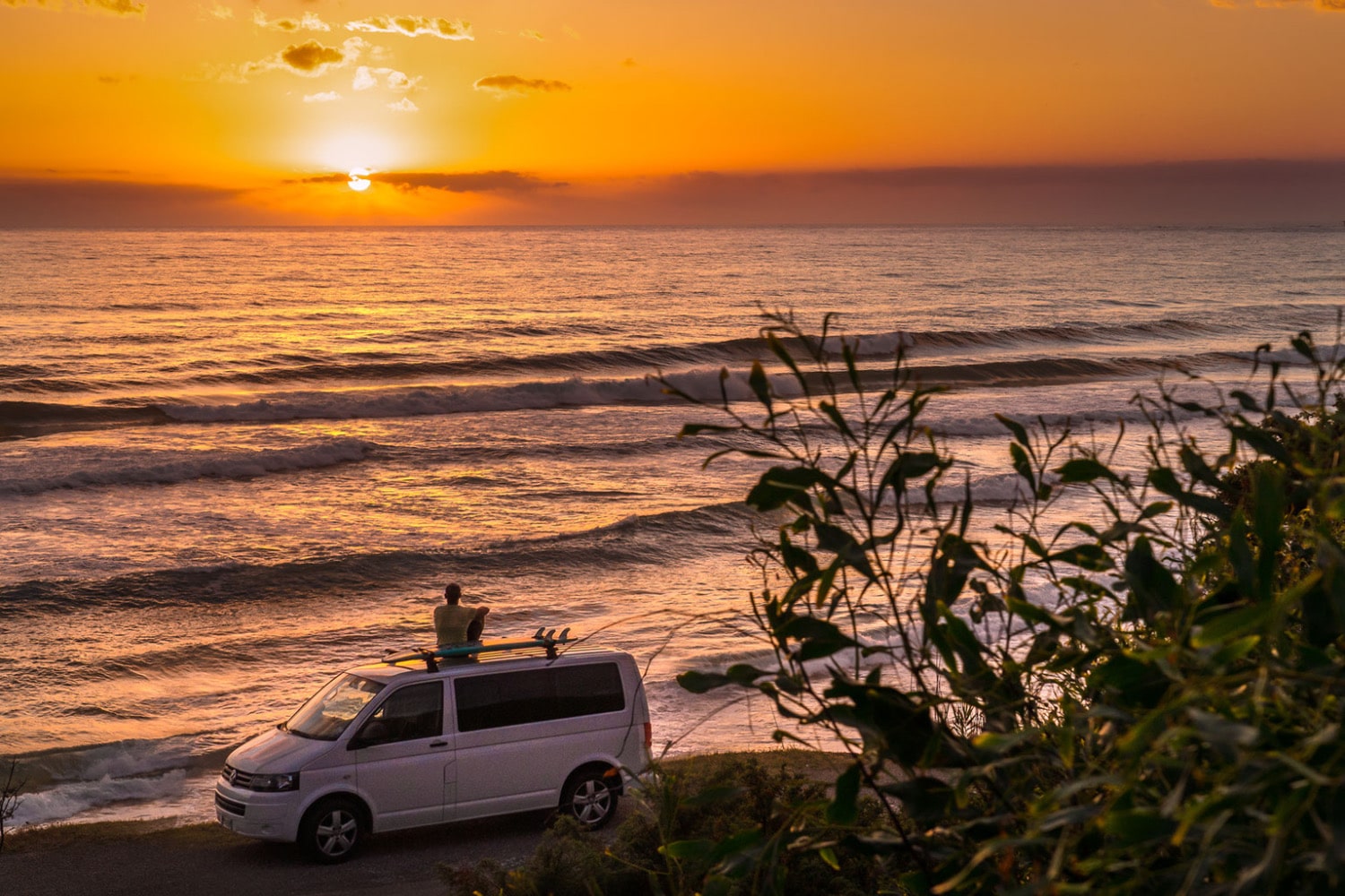 Un homme adepte de la vanlife regarde un coucher de soleil sur le toit de son véhicule aménagé.