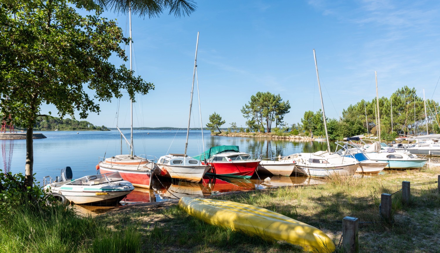 Voiliers et petits bateaux de plaisance amarrés sur le lac de Lacanau entouré de pins